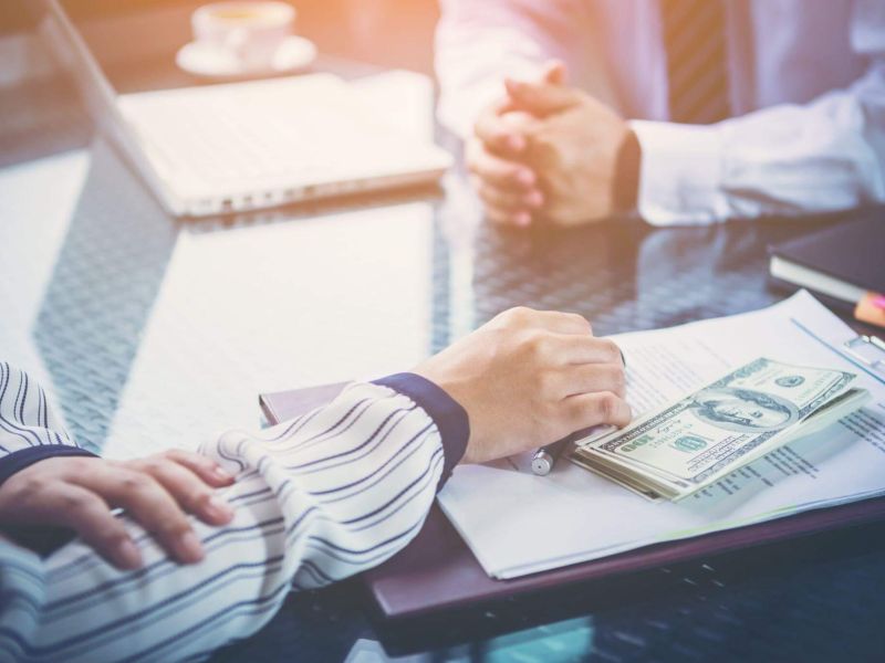 two people sitting at a table with a notebook and money