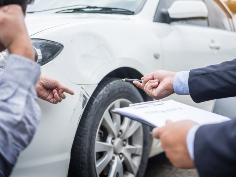 Man inspecting car damage with clipboard and pen, discussing accident details.