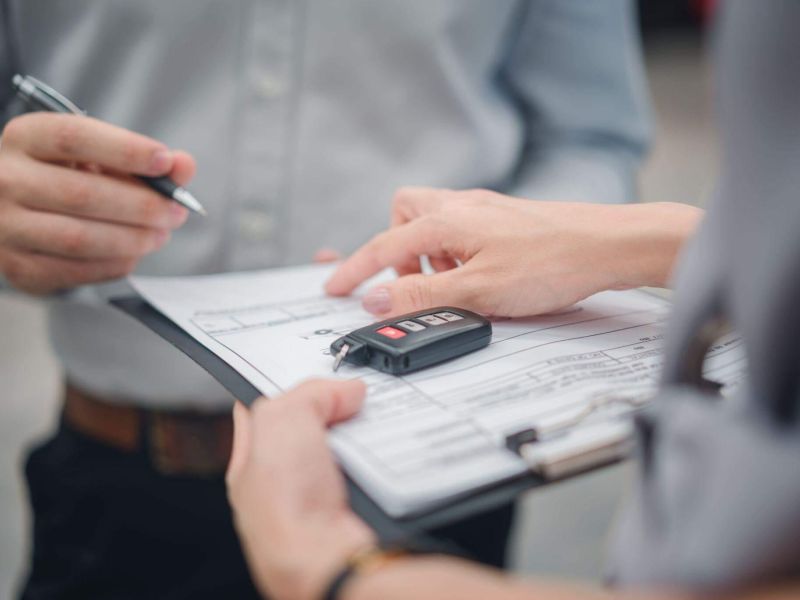 a person holding a clipboard with a car key while another person holds a pen