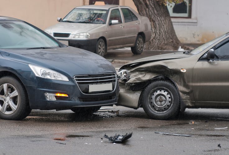 Two cars in a frontal collision on a city street, showing damaged bumpers and headlights.